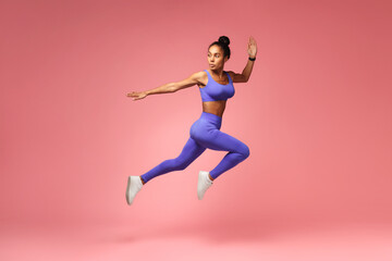 Fototapeta na wymiar Athlete african american lady jumping having workout on pink background