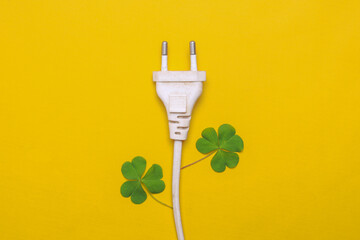 Creative flat lay of electrical plug and fresh green leaves on yellow background. Save energy and earth hour concept