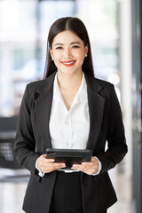 Smiling confident business woman leader standing in office, holding digital tablet and looking at camera