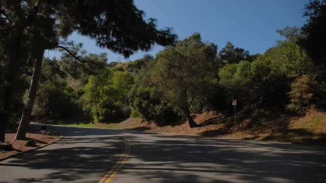 POV wide shot of car Driving rural road on Hollywood hill to sign and observatory on sunny day. California, USA