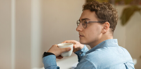 Calm millennial european guy student in glasses drink tea, enjoy coffee cup