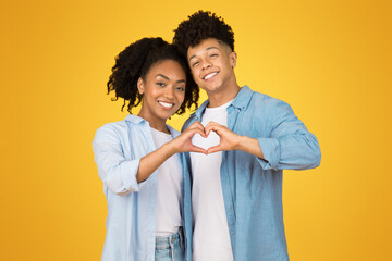 Smiling young african american guy and woman in casual make heart sign with hands