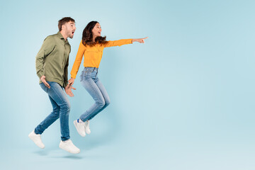 Excited couple jumping and pointing at free space on blue background