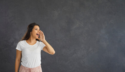 Woman standing on gray background loudly announces advertising, news or information about discounts. Caucasian casual young woman looking towards free space for text. Advertising concept. Banner.