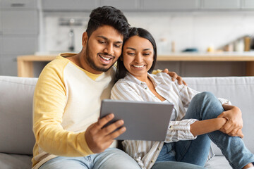Happy Indian Couple Watching Videos On Digital Tablet While Relaxing At Home