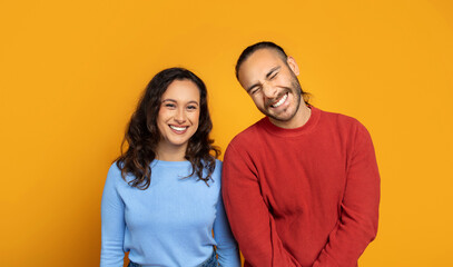 Cute millennial couple posing together on orange background
