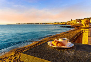 Fototapeta na wymiar concept of street outdoor breakfast with a cup of tea or coffee on a morning coast during sunrise. landscape of city embarkment with sea water and cloudy sky on background