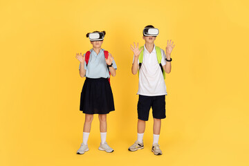 Two school children with backpacks are wearing virtual reality headsets, standing with arms raised