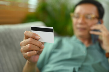 Select focus on senior man holding bank plastic card and talking on mobile phone