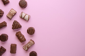 Flat lay of assortment of delicious chocolate candies on pink background. Flat lay, top view. Space for text. 
