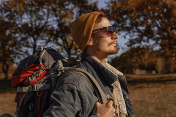 Side view of male traveler with hiking backpack in sunglasses and hipster wear standing on sunny...