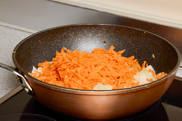 A wok with onion, bell pepper and carrot cooking on the stove