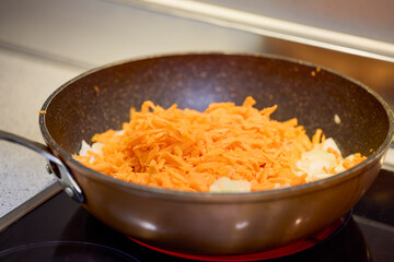 A wok with onion, bell pepper and carrot cooking on the stove