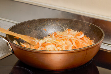 A wok with onion, bell pepper and carrot cooking on the stove