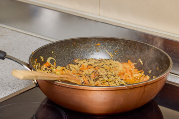 A wok with Rice, onion, bell pepper and carrot cooking on the stove