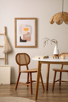 Creative composition of dining room interior with round table, rattan chair, wooden commode, pock up poster and kitchen accessories. Beige wall with mock up poster. Home decor. Template.