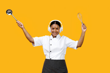 Smiling black female chef dancing with kitchen utensils in hands