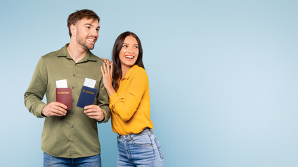 Excited couple holding passports and looking at free space on blue background