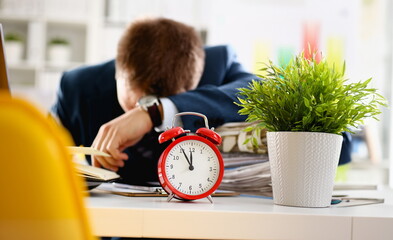 Red alarm clock shows late time closeup and tired office male clerk in suit take nap on table...