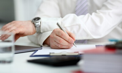 Male arm in suit and tie hold silver pen filling schedule in notepad at office workplace closeup....