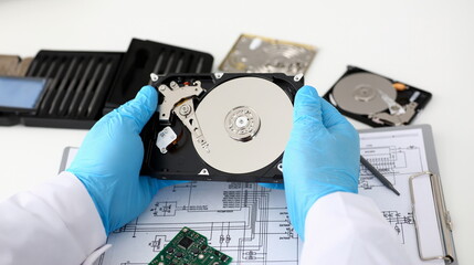A male repairman wearing blue gloves is holding a hard drive from computer or laptop in hands....