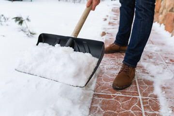 A man removes snow with a shovel from the path near the house