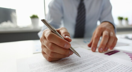 Hand of businessman in suit filling and signing with silver pen partnership agreement form clipped...