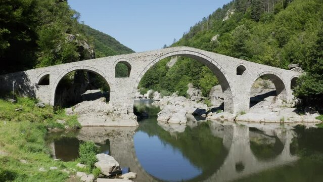 Approaching drone shot going through the Devil's Bridge over the Arda River located in the town of Ardino at the foot of Rhodope Mountain in Bulgaria.