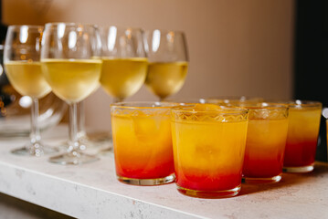 Tequila Sunrise and White Wine Selection. An array of Tequila Sunrise cocktails with gradient orange hues and white wine in stemmed glasses, ready for a party.