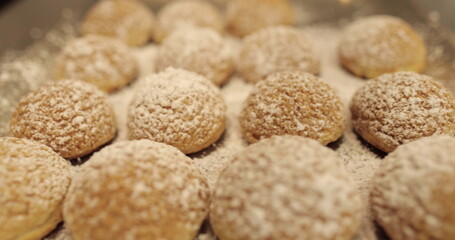 Ready-made cakes sprinkled with powdered sugar are stacked in even rows on a metal tray in a professional pastry shop.