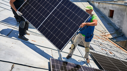 Workers building solar panel system on metal rooftop of house. Two men installers carrying...