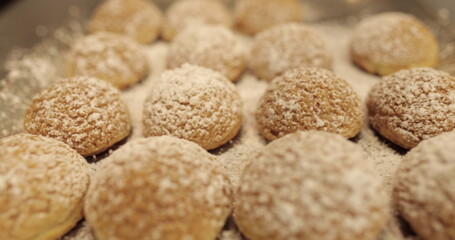 Ready-made cakes sprinkled with powdered sugar are stacked in even rows on a metal tray in a professional pastry shop.