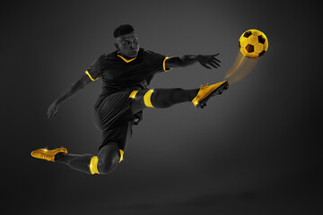 Black and yellow color combination. Young man, football player in motion kicking ball with leg in...