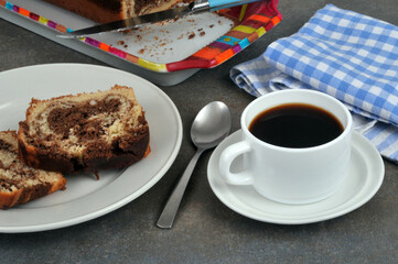 Tasse de café avec une cuillère et des tranches de cake marbré dans une assiette.​