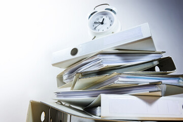Alarm clock on stacked ring binders against a gray background threatened to deadline ultimatum,...