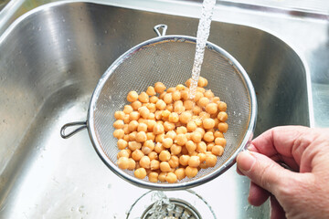 Pre-cooked canned chickpeas are rinsed with water in a sieve over the sink before being used in various dishes, healthy legumes are rich in protein, fiber and minerals, copy space