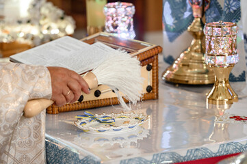 The priest sprinkles the golden cross with holy water.