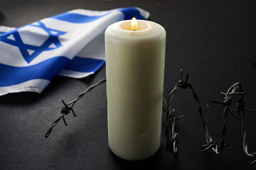 Flag of Israel, barbed wire and burning candle on black background. Holocaust memory day