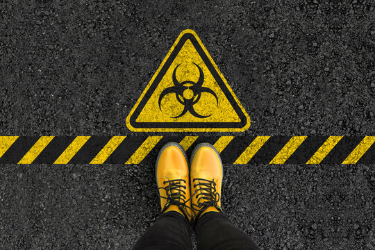 legs in boots standing on asphalt road and biohazard sign 