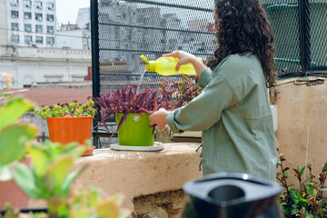 young woman in terrace garden placing water on plants with plastic container.