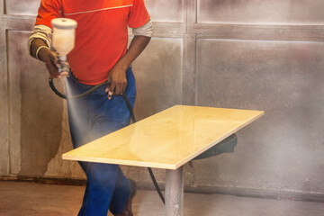 african carpenter using a spray painting gun to paint a plank