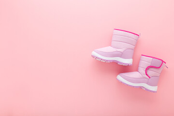 New warm waterproof winter boots on light pink table background. Pastel color. Children footwear....