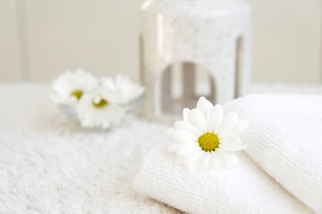 Fototapeta na wymiar White towels with chamomile flower and aroma lamp, candle on background. Spa and wellness or beauty salon, romantic relaxation concept. Intimate hygiene. Copy space.