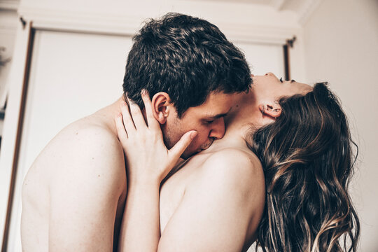 Young passionate couple (two lovers) kissing on the neck for intense sex in the bedroom, young tender lover touching the skin of a sexy sensual lady moaning and making love. Foreplay concept.