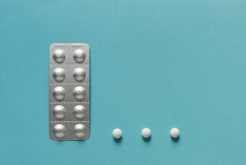Medicine blister strip and three round white pills on a plain blue background. Pharmacy products....