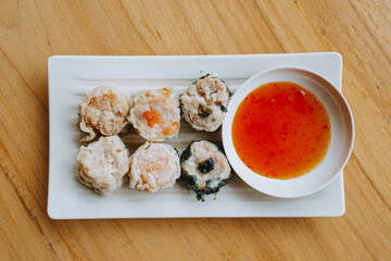 A plate of Dim Sum with chili sauce on wooden table. Flat lay or top view shot.