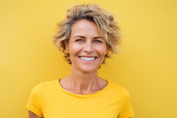 Portrait of a smiling middle-aged woman with short hair standing against yellow background