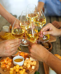 Hands with white wine toasting over served table with food