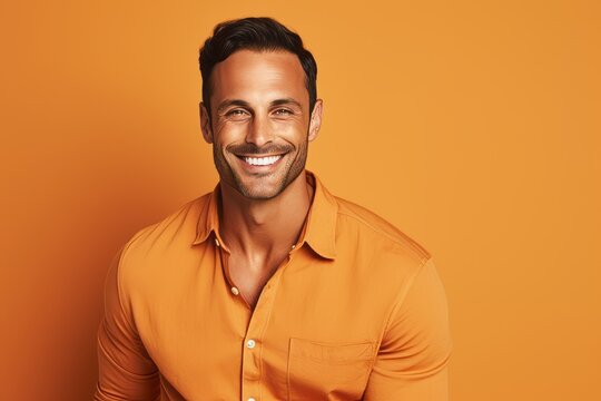 Handsome man in orange shirt smiling at camera while standing against orange background