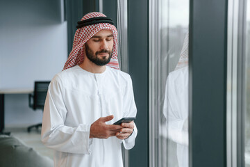 In the office with phone. Successful Muslim businessman in traditional outfit
